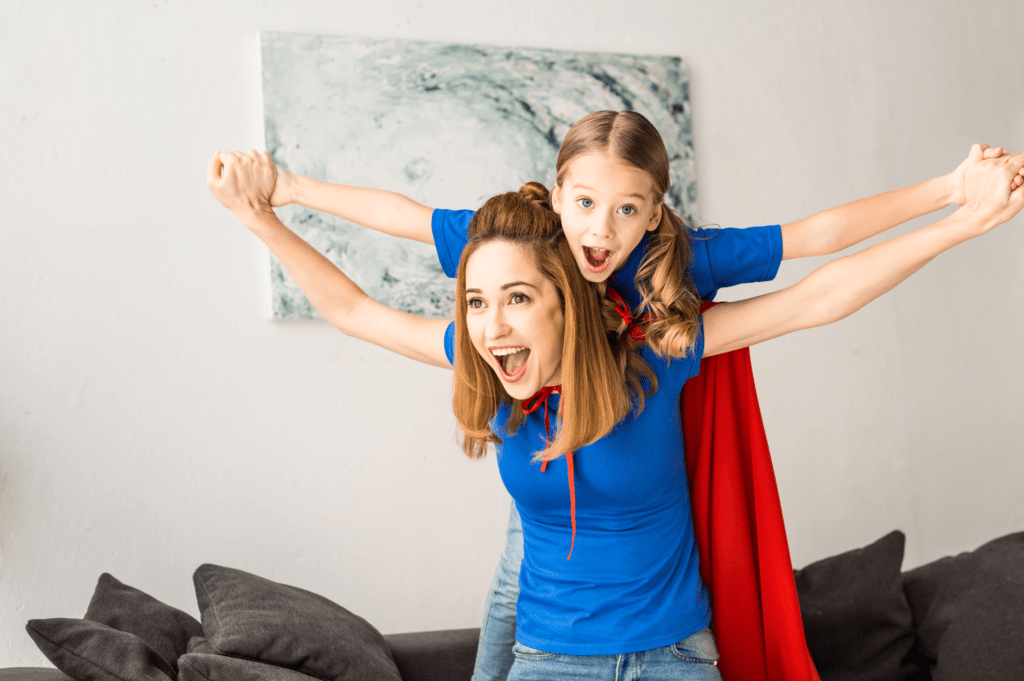 Woman dressed as super hero with daughter on her back. Super Mom doesn't have any doubts about being a stay at home mom vs. working mom.