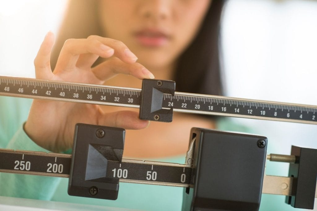 Woman weighing herself and tracking  it on her weight loss chart.