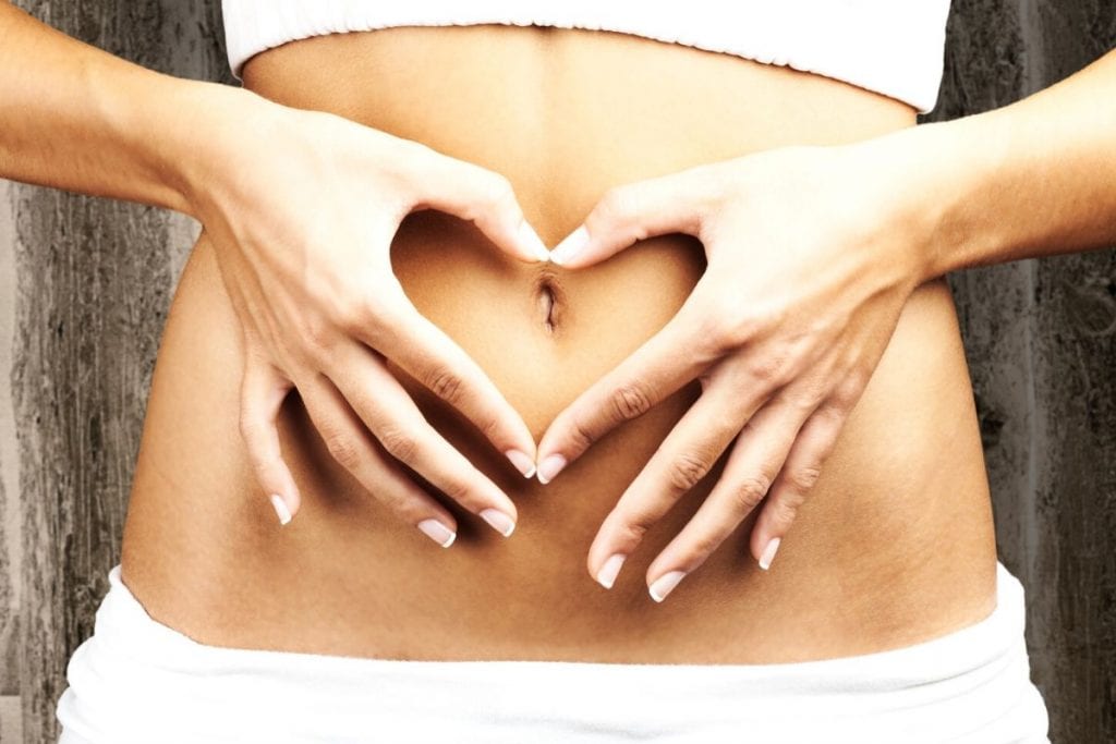 Woman with hands to belly making a heart because she takes Arbonne Digestion Plus.