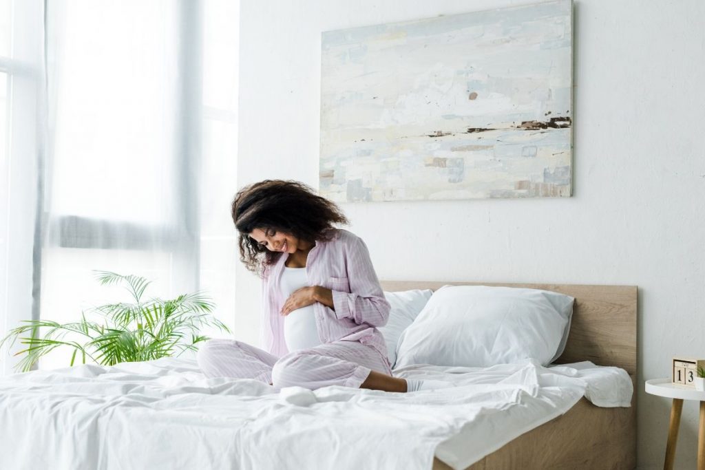 Pregnant woman practicing pregnancy affirmations in bed, smiling at her belly.