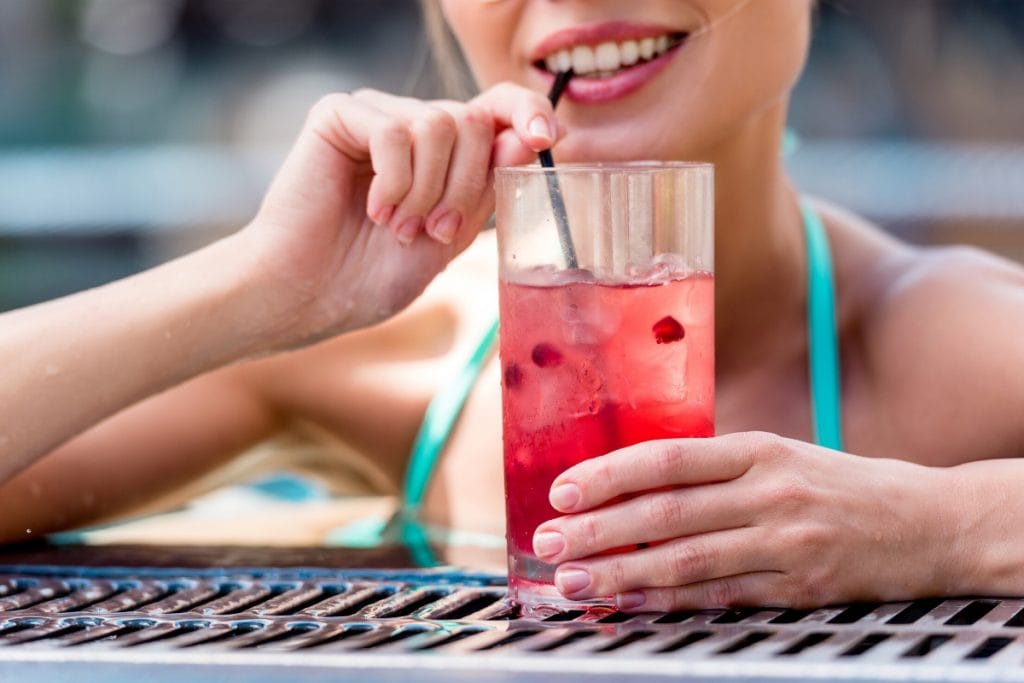 Woman drinking pomegranate Arbonne fizz stick with ice by the pool