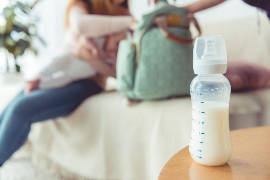 Close-up on baby bottle with mom who is feeling depressed about going back to work after maternity leave in the background.