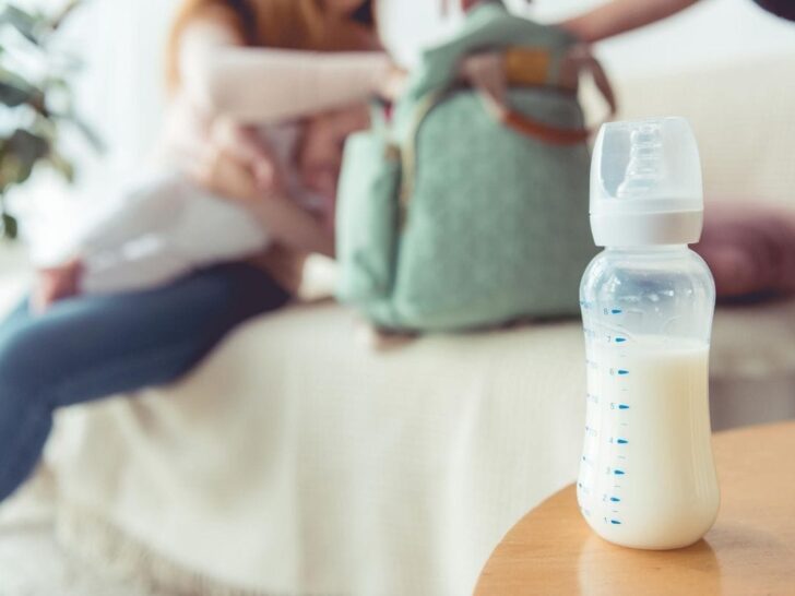 Close-up on baby bottle with mom who is feeling depressed about going back to work after maternity leave in the background.