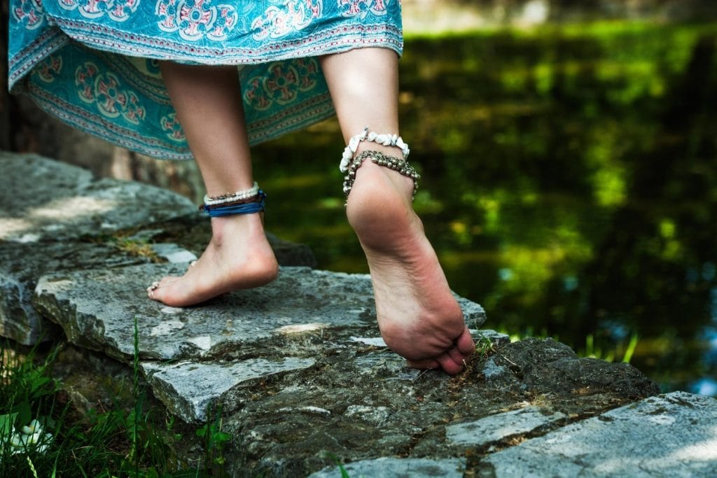 Woman walking along stones with bare feet.