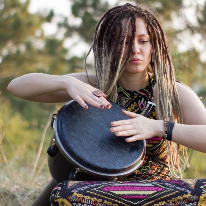 Woman with dreadlocks playing an African drum.