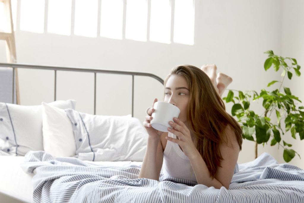 Woman drinking coffee in bed saying positive, morning affirmations to herself