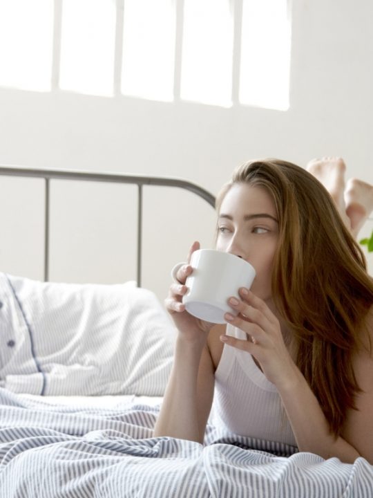 Woman drinking coffee in bed saying positive, morning affirmations to herself