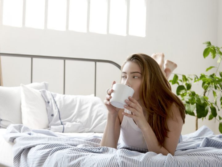 Woman drinking coffee in bed saying positive, morning affirmations to herself