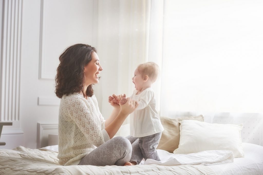 Stay at home mom with her baby on a bed, smiling and dancing.