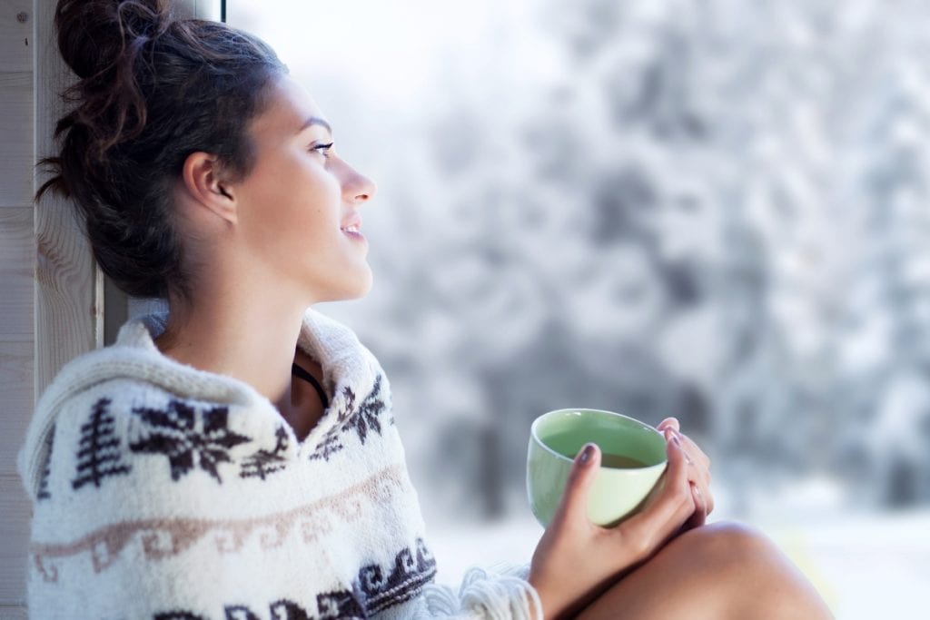 Woman looking longingly out the window with tea in hand