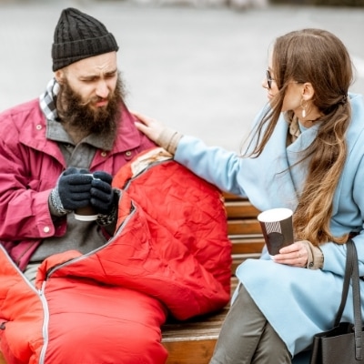 Woman talking to a homeless man and giving him and cup of coffee. Finding ways to give back or be kind to others is a great way to nourish your soul