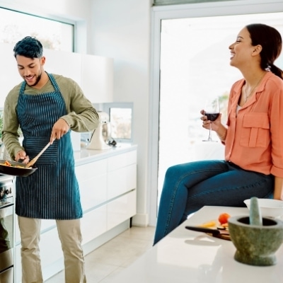 Man cooking in the kitchen with woman sipping red wine.