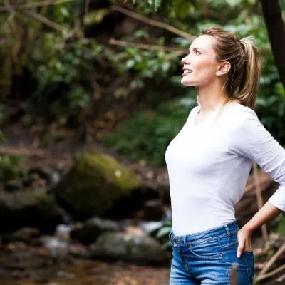 Woman with a ponytail hiking in nature and staring wistfully at the trees
