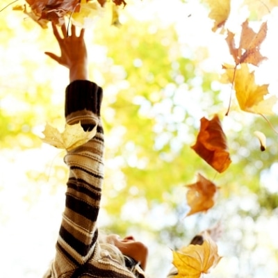 Woman throwing leaves into the air and light symbolizes letting go of control and expectations