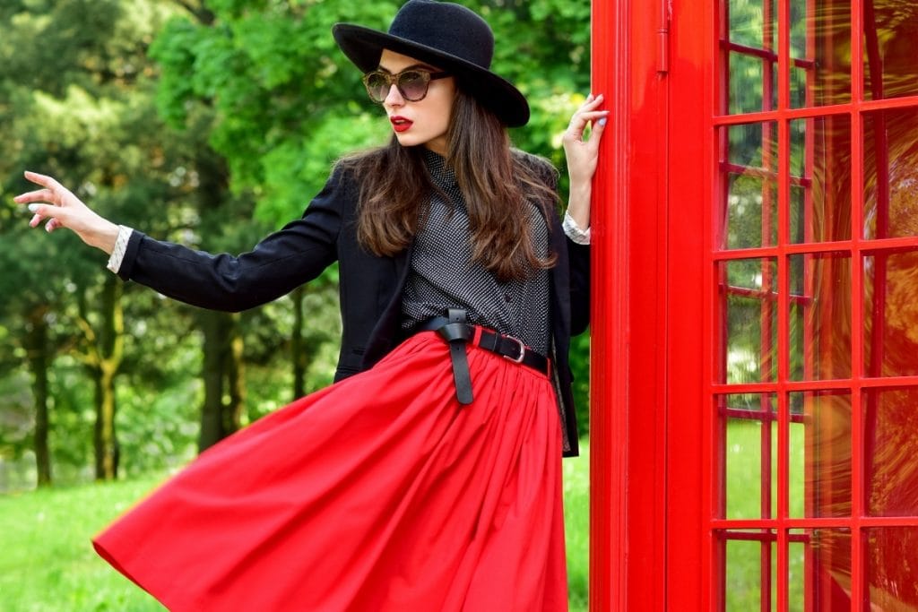 Woman in bright red skirt posing near a red building.