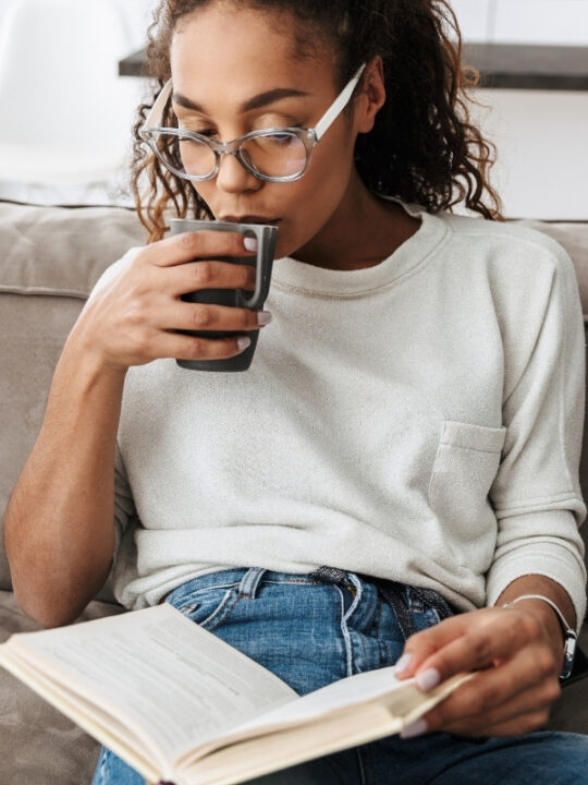 Woman reading best female empowerment books on her sofa sipping tea
