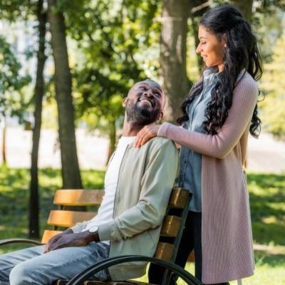 Woman standing above a man seated on a park bench, looking at each other lovingly