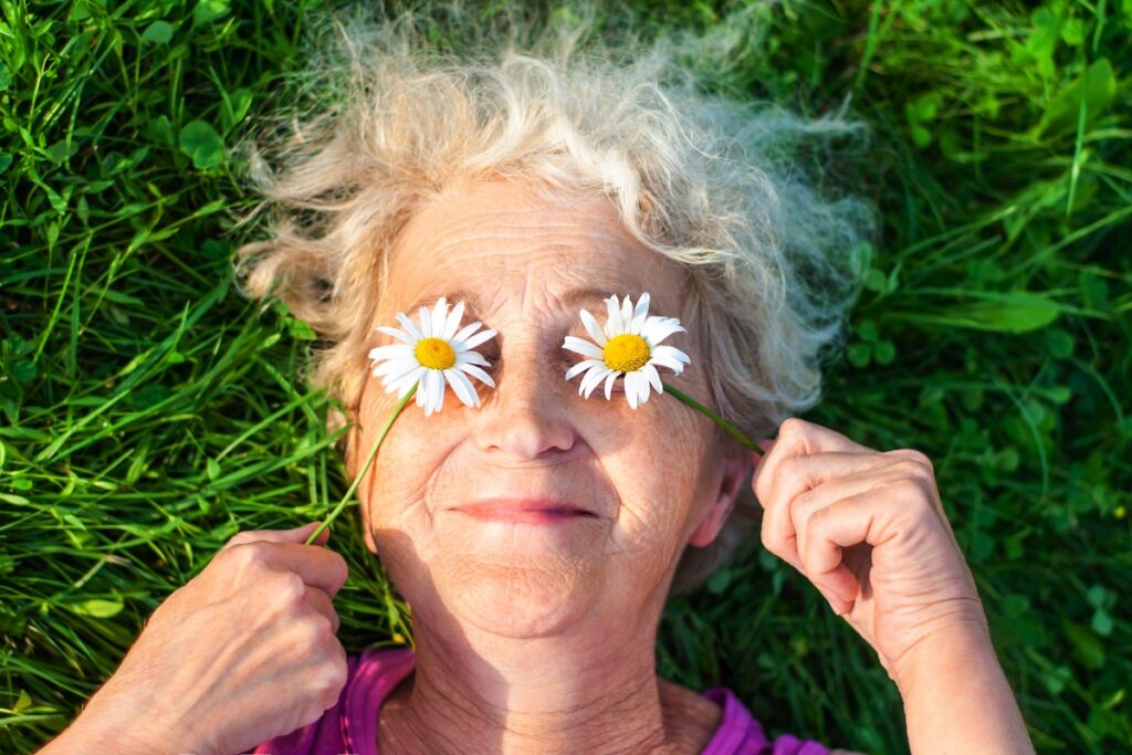 Older woman with lovely smile holding daisies over her eyes