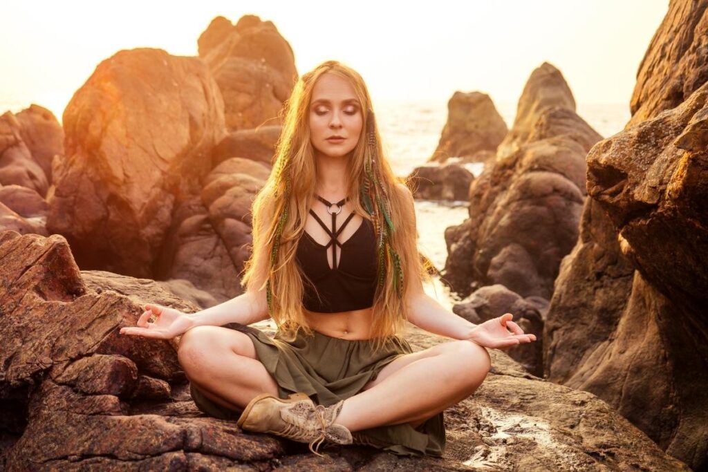 Buddhist witch meditating on some rocks wearing boho attire