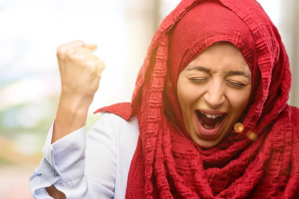 Woman in hijab practicing self-celebration with excited gesture and smile
