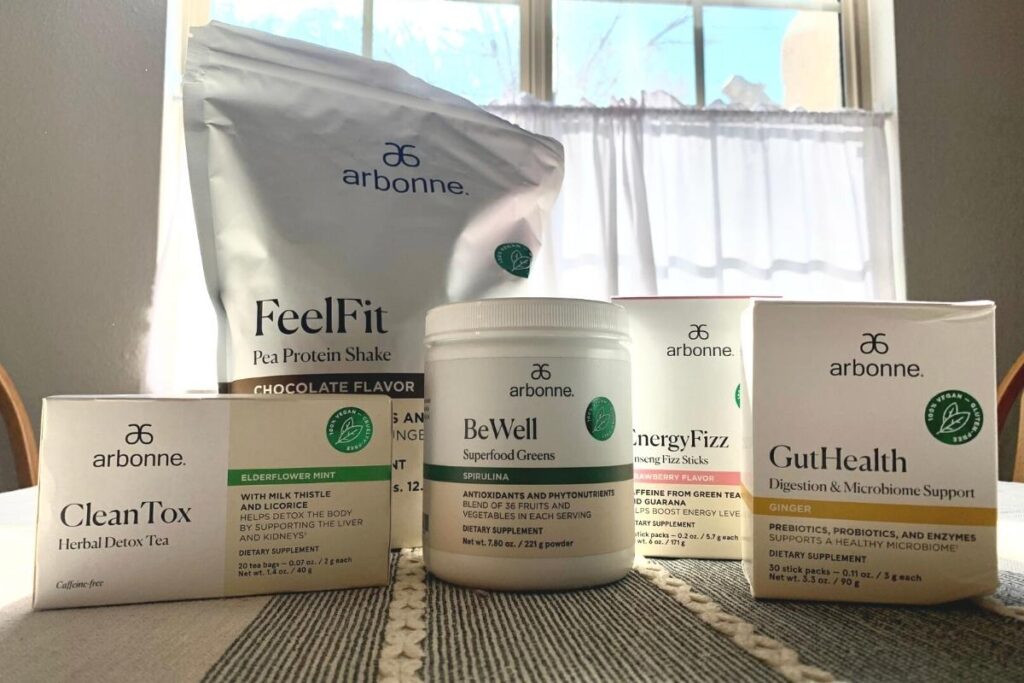 Arbonne Protein powder, Detox tea, BeWell Greens, Gut Health, and Energy Fizz Sticks on a table. These Arbonne Nutrition products are all part of the Arbonne 30 Days to Healthy Living Package