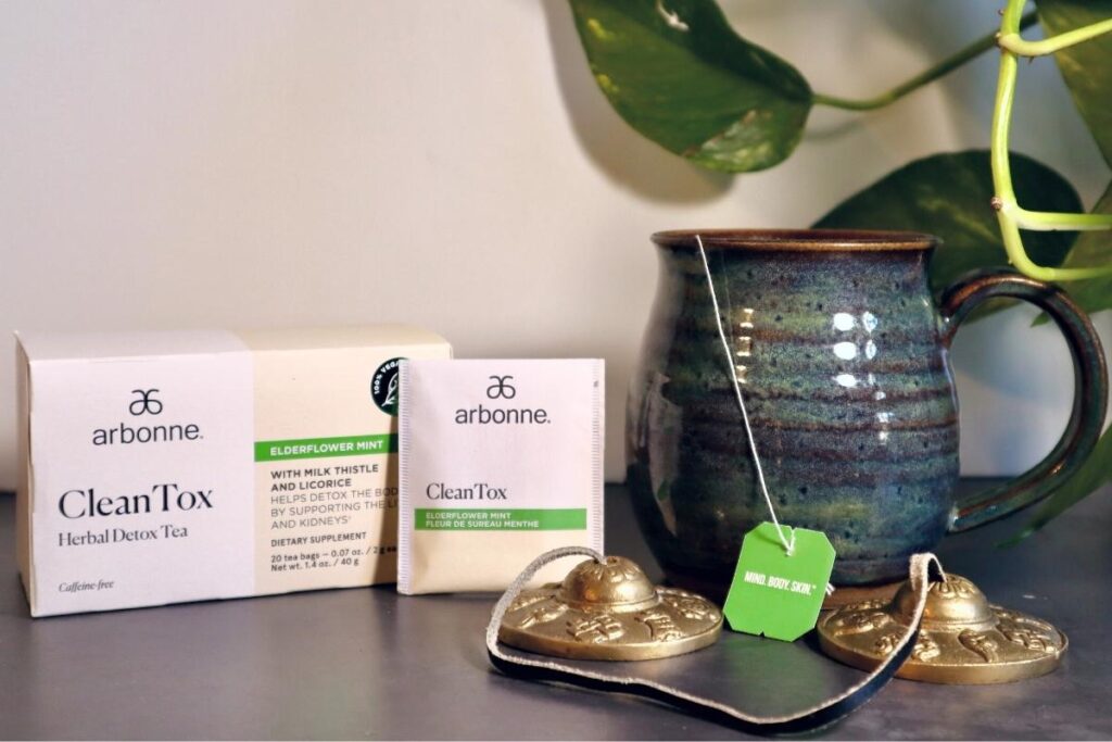 Styled photoshoot of Arbonne Clean Tox Herbal Detox Tea with Box, tea bag, and mug with steaming tea