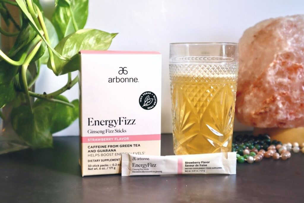 Styled photoshoot of Arbonne Energy Fizz Sticks Strawberry Flavor with box, packet, and crystal glass with fizz mixed with water