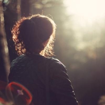 Woman looking at sun through the forest. When going through a spiritual awakening, you may feel alone in the world