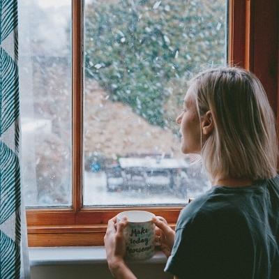 Woman looking longingly out the window with a cup of tea