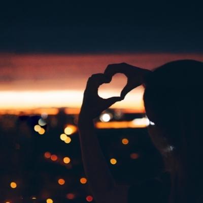 Woman making a heart with her hands in front of the sunset