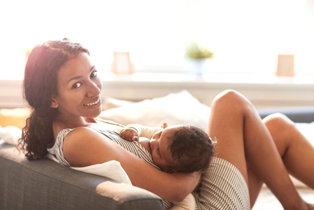 Woman using affirmations for breastfeeding while chestfeeding baby on a couch.