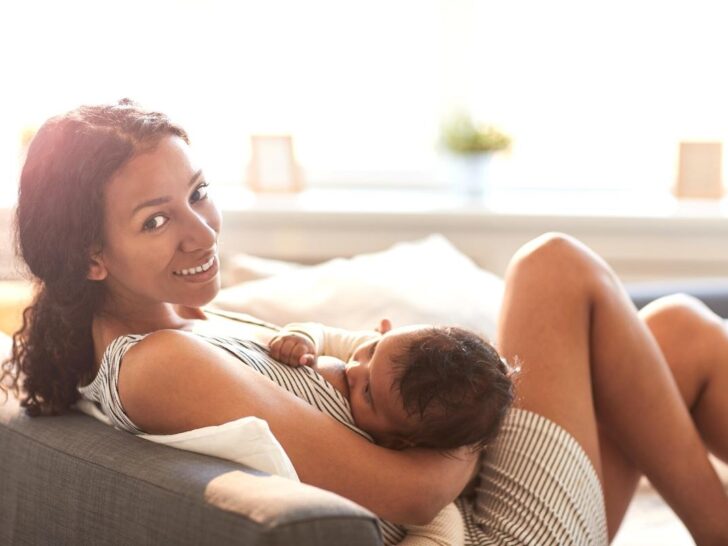 Woman using affirmations for breastfeeding while chestfeeding baby on a couch.