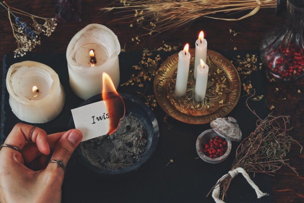 A woman using a witch protection spell at her altar with candles, herbs, and paper with intentions