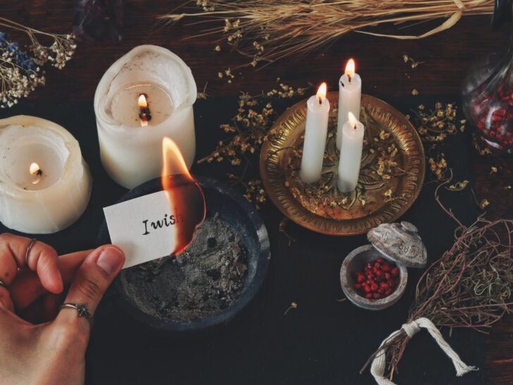 A woman using a witch protection spell at her altar with candles, herbs, and paper with intentions