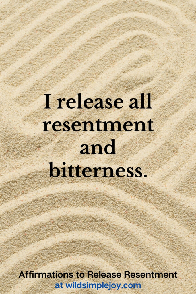 Vertical Pinterest Image with sand background and text overlay that reads I release all resentment and bitterness Affirmations to release resentment at wildsimplejoy.com