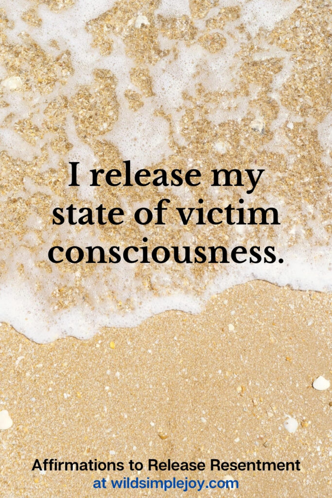 Vertical Pinterest Image with sand background and text overlay that reads I release my state of victim consciousness Affirmations to release resentment at wildsimplejoy.com