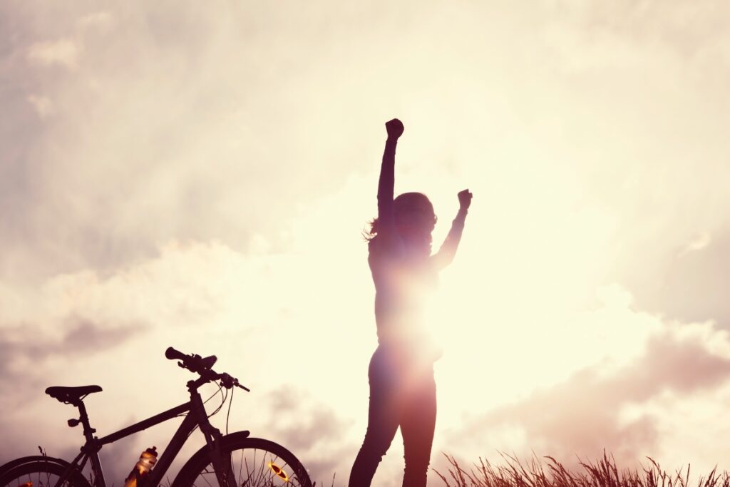 Woman in sunset raising her arms in celebration and success