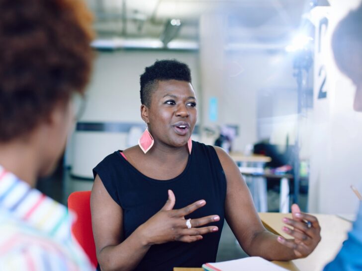 Woman in black top with large red earrings explaining something to others in conversation