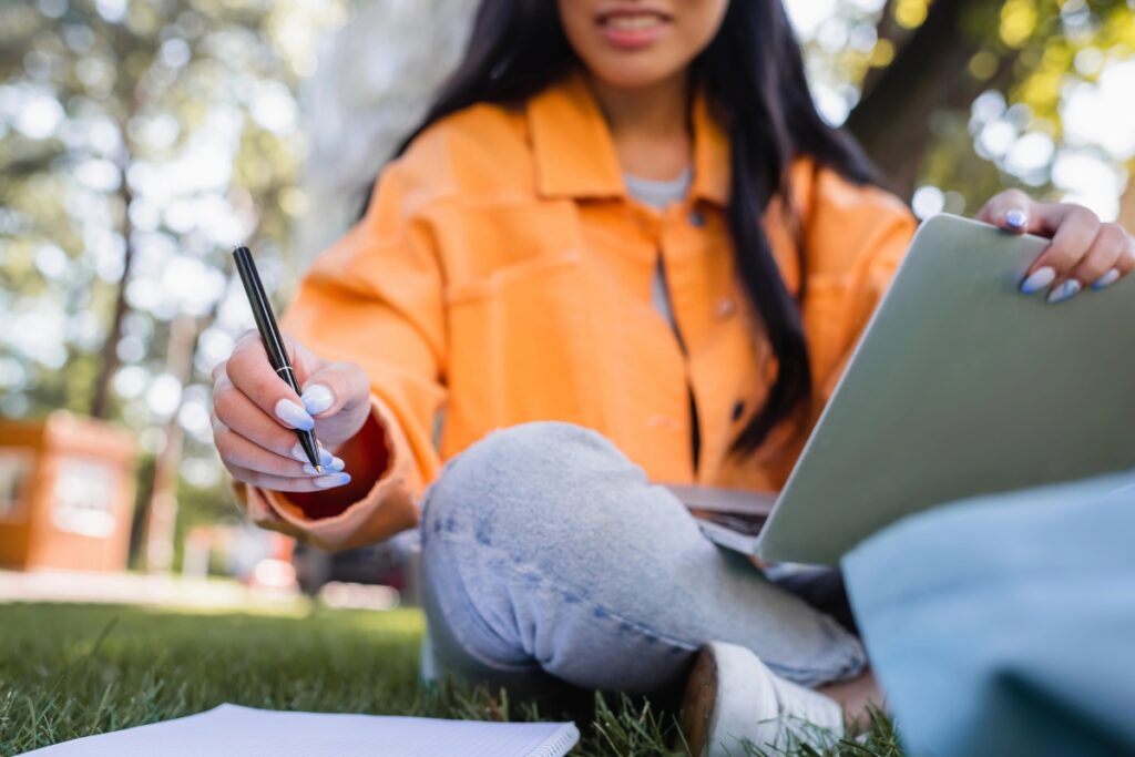 Woman in orange jacket writing in a journal with an ipad or tablet